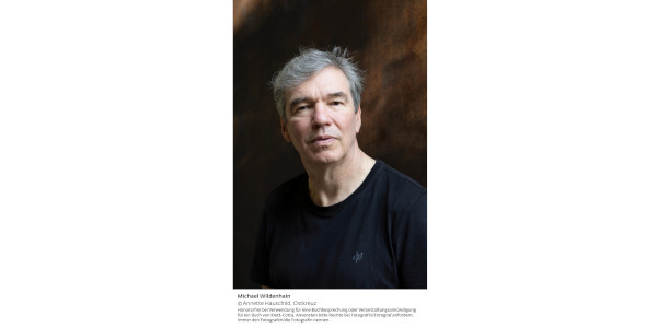 Portraitfoto vom Autor Michael Wildenhain, einem Mann mittleren Alters mit grauen Haaren in blauem Pullover.